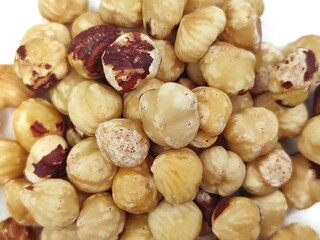 Closeup view of a pile of roasted, unsalted hazelnuts, isolated on white background.