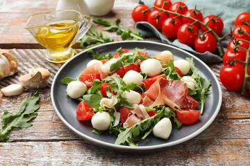 Tasty salad with arugula, mozzarella cheese, tomatoes and jamon on wooden table, closeup