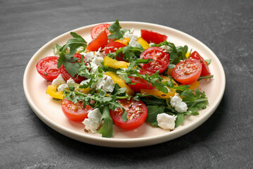 Tasty salad with arugula, cheese and vegetables on dark textured table, closeup