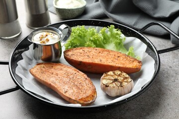 Tasty cooked sweet potato in baking dish served on grey textured table