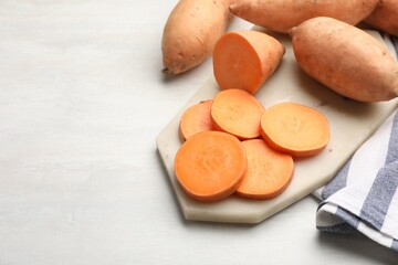Fresh sweet potatoes and kitchen towel on white table, closeup. Space for text