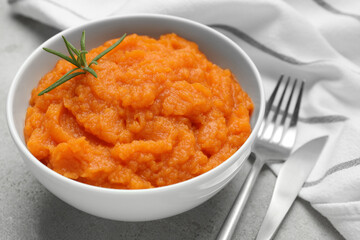 Tasty mashed sweet potato with rosemary in bowl served on grey textured table, closeup