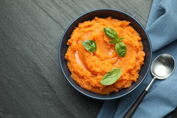 Tasty mashed sweet potato in bowl served on dark gray textured table, flat lay