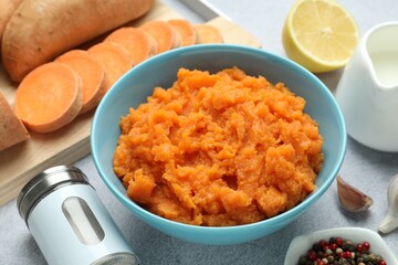 Tasty mashed sweet potato in bowl, fresh vegetables, spices, sauce and lemon on gray table, closeup