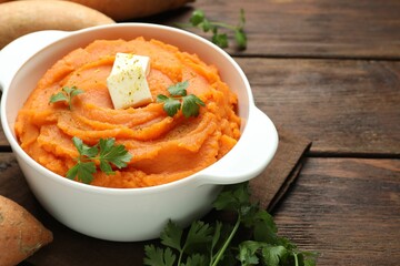 Tasty mashed sweet potato with butter and parsley in bowl on wooden table, closeup