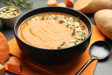 Delicious sweet potato soup with pumpkin seeds in bowl and vegetables on grey table, closeup