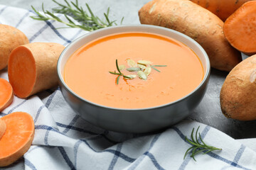 Delicious sweet potato soup with pumpkin seeds in bowl, vegetables and rosemary on table, closeup