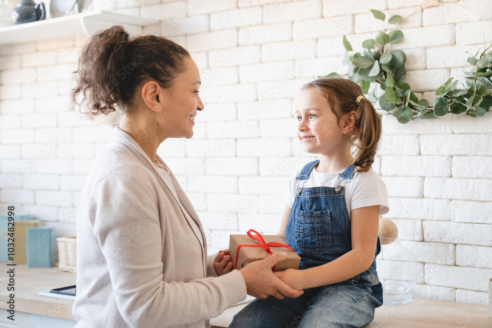 Wall mural Holiday event celebration. Caucasian mother giving receiving present gift box to her small daughter girl in the kitchen, celebrating Christmas New Year Mother`s Day birthday together.