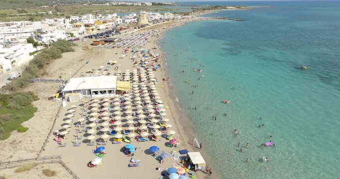 Aerial view of Torre Mozza beach in Salento, Puglia, Italy. There are people in the water and on the beach. In the background a coastal tower. Holiday concept.