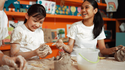 Caucasian highschool girl modeling cup of clay while looking smart boy in art class at workshop....