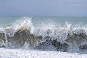 The ocean is rough and the waves are crashing against the shore. The sky is cloudy and the water is a deep blue color