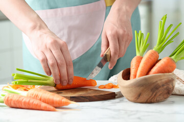 Woman cutting fresh carrot at white marble table, closeup