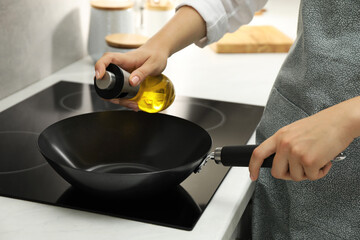 Woman with bottle of oil and frying pan in kitchen, closeup
