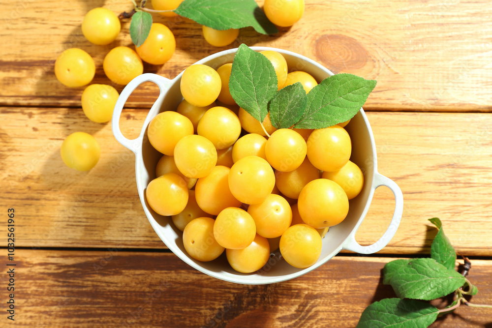 Poster Tasty ripe plums and leaves in colander on wooden table, flat lay