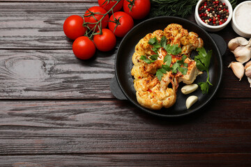 Tasty cauliflower steak in frying pan and other products on wooden table, top view. Space for text