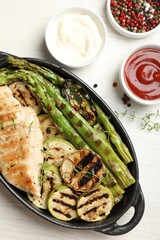 Delicious grilled vegetables and chicken breast in baking dish on white wooden table, flat lay