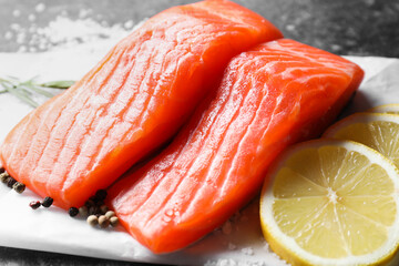 Pieces of fresh salmon with lemon and peppercorns on dark table, closeup