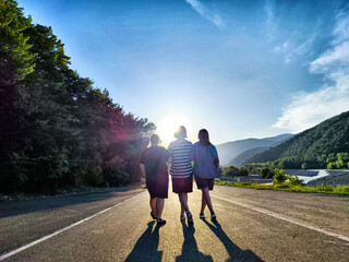 Three individuals stroll down a picturesque road under a bright sun