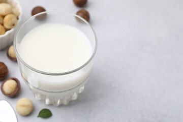 Glass of macadamia milk and nuts on white table, closeup. Space for text