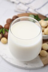 Glass of macadamia milk and nuts on white tiled table, closeup