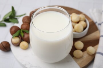 Glass of macadamia milk and nuts on white table, closeup