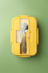 Yellow lunch box with cutlery on green background, top view