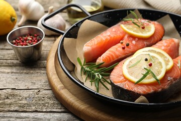 Fresh raw salmon steaks with spices in pan on wooden table, closeup