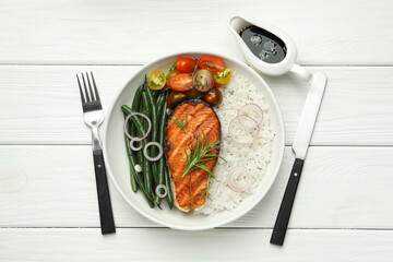 Tasty grilled salmon steak with rice and vegetables served with soy sauce on white wooden table, flat lay