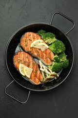Tasty grilled salmon steak with lemon and vegetables on dark textured table, top view