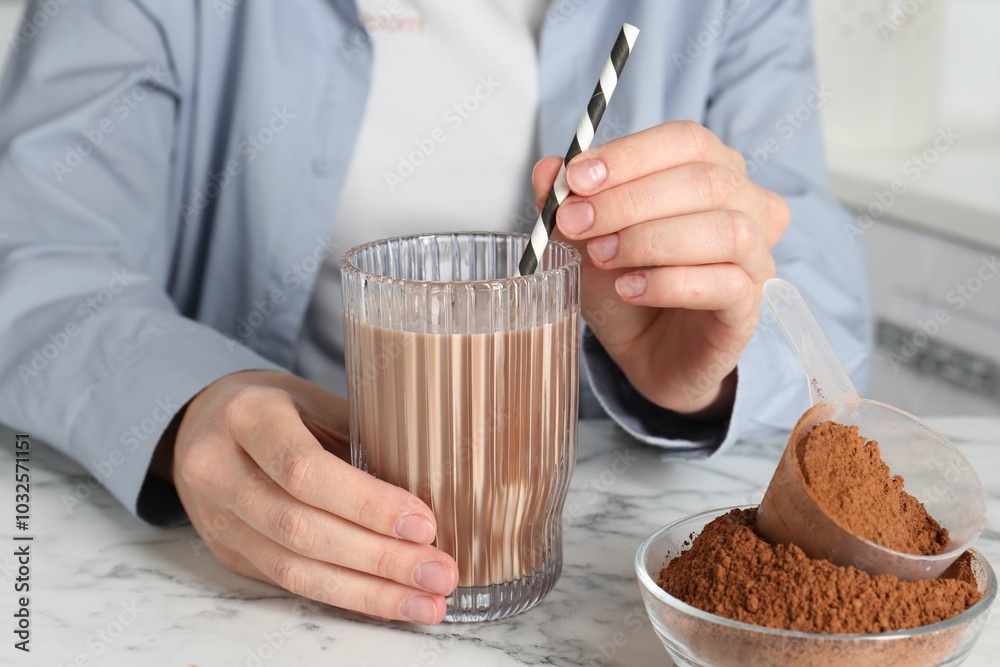 Wall mural Woman with glass of protein cocktail and powder at white marble table, closeup