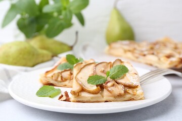 Pieces of tasty puff pastry pie with pears and mint on light grey table, closeup