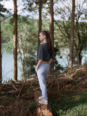 Young woman standing on a tree stump in a serene forest, gazing thoughtfully at the river Nature and self reflection concept in a tranquil setting