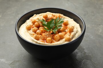 Delicious hummus with parsley, paprika and chickpeas in bowl on grey table, closeup