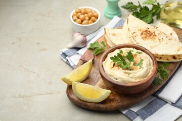 Delicious hummus with parsley, paprika, pita, chickpeas and lemon on grey table, space for text