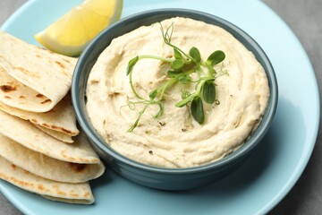 Delicious hummus in bowl, pita and lemon on table, closeup