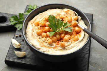 Delicious hummus with parsley, paprika and chickpeas on grey table, closeup