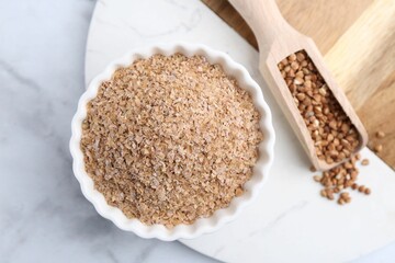 Buckwheat bran in bowl and grains on white marble table, top view