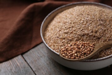 Buckwheat bran in bowl and grains on wooden table, closeup. Space for text