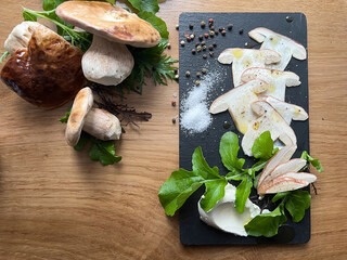 Porcini mushroom carpaccio seasdoned with salt, pepper and olive oil. Fancy fresh forest dish served on a black stone on wooden background.