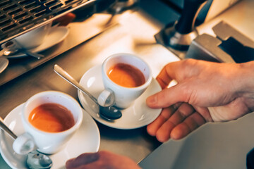 Barista holding two cups of freshly brewed espresso are being served in a charming café. The warm, inviting atmosphere enhances the coffee experience during a pleasant afternoon.
