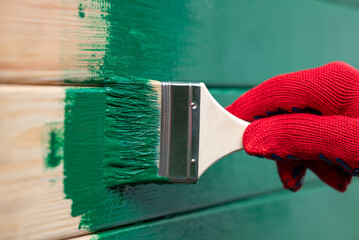 Painting wall in green color. Applying dye to wooden wall of a house with brush