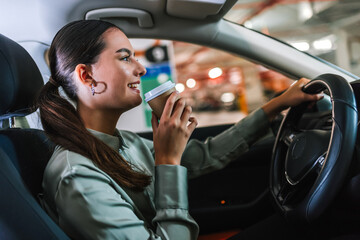 Young woman searching for parking spot in underground garage. Driving around in her car and drinking coffee.