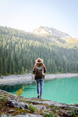 Time for solitude. Happy tourist woman enjoys the view of the mountain lake in sunny weather. Woman sitting on a rock in the mountains, resting on a halt on a hike.