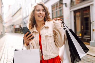 Happy Woman use mobile phone and hold shopping bag. Black Friday. Sale. Online shopping.