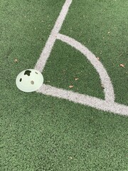 A close-up shot of a corner area on a green sports field marked with white lines, most likely a soccer field. A light green plastic training cone is placed near the corner line.