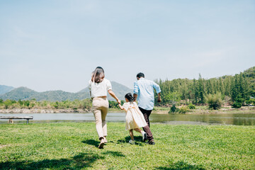 Asian family father mother and daughter holding hands and running lake in park, lifestyle parents and child kid enjoying outdoors together in nature on summer travel, Family relaxation, Back view