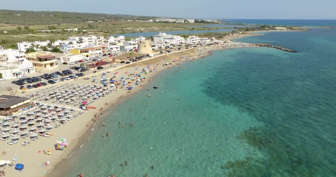 Aerial view of Torre Mozza beach in Salento, Puglia, Italy. There are people in the water and on the beach. In the background a coastal tower. Holiday concept.