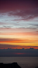 City skyline with buildings silhouetted against vibrant sunrise over the sea. Aerial view at dusk
