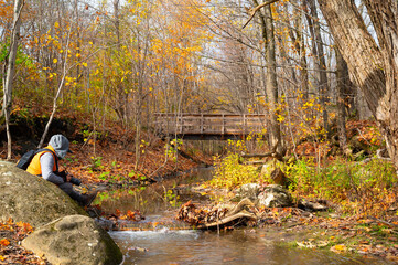 Person sitting on a rock by a small river in the autumn forest