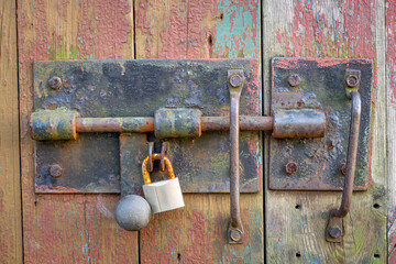 old bolt on a barn door in the countryside. rusty padlock on rusty metal. primitive gate closing. old ugly colorful boards